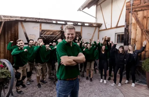 Eine Gruppe von Handwerkern in grüner Arbeitskleidung steht motiviert vor einem Firmengebäude.