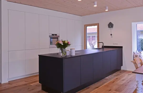 Moderne Einbauküche mit Kochinsel, Holzboden und weißen sowie dunklen Küchenfronten.