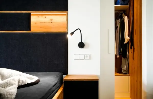 Modernes Schlafzimmer mit gemütlichem Bett, Leselampe und offenem Kleiderschrank aus Holz.