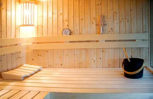 Moderne Sauna aus hellem Holz mit Thermometer, Saunakübel und Kopfstütze auf der Bank.